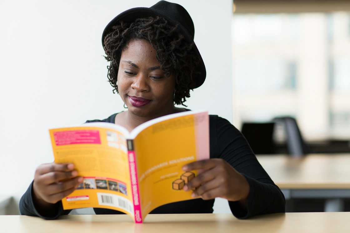 A woman in a black long-sleeved top and a black hat is reading a book with a yellow cover A woman in a black long-sleeved top and a black hat is reading a book with a yellow cover