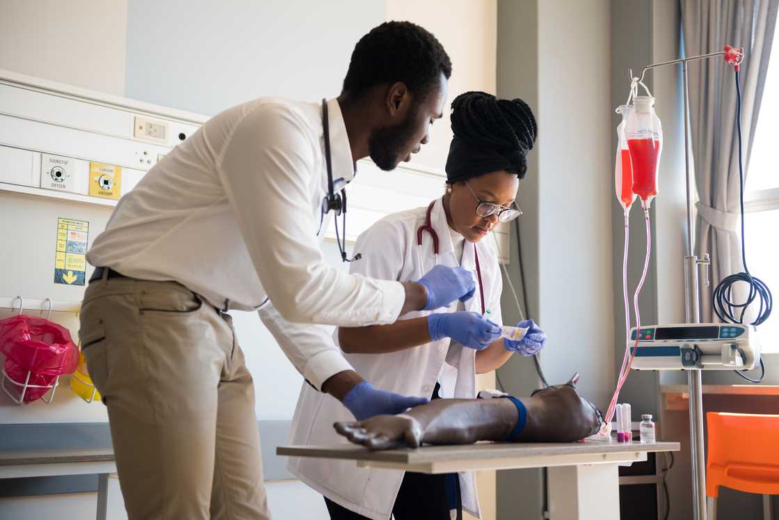 Young male and female doctors practicing IV Drip on artificial limb Young male and female doctors practicing IV Drip on artificial limb