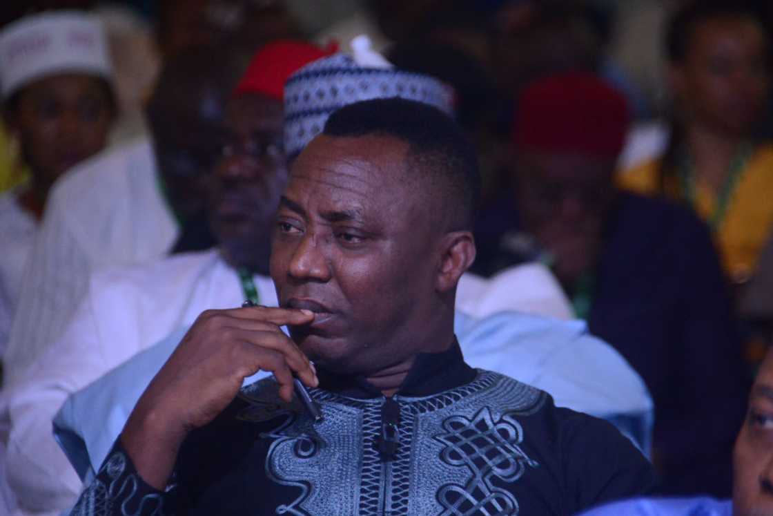 Omoyele Sowore in a blue embroidered agbada and cap, seated during the national anthem at the signing of the National Peace Accord in Abuja, 2022