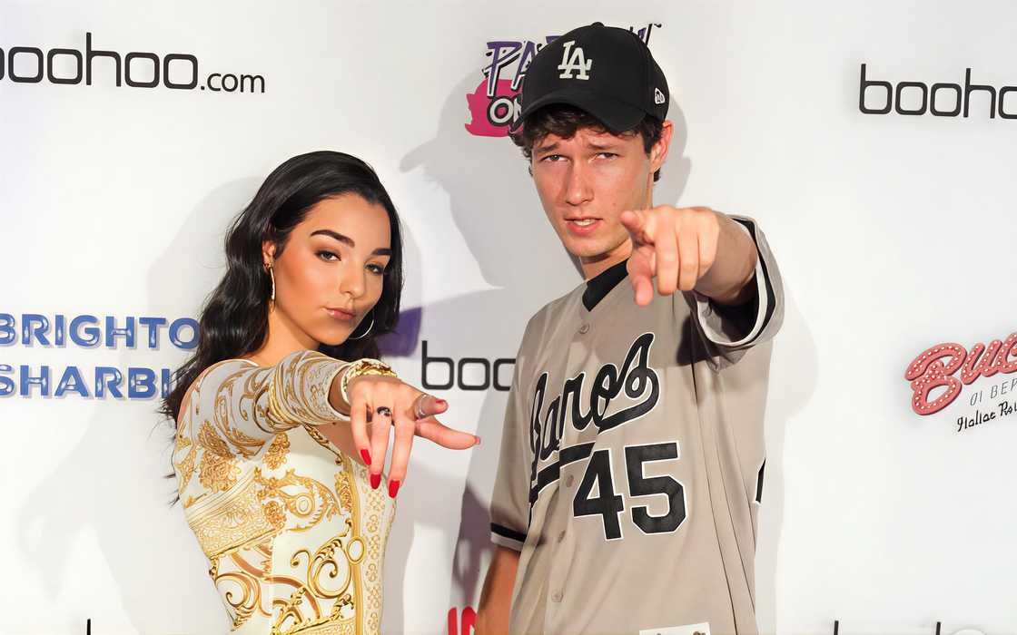 Indiana Massara wearing a patterned gold-and-white dress and Zach Justice a grey baseball jersey with an LA cap