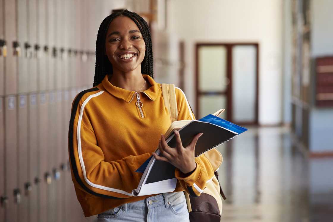 A female student standing with books in hallway at high school.