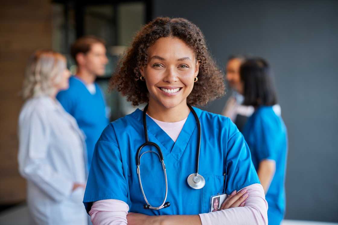 A nurse smiling with crossed arms with healthcare team in background. A nurse smiling with crossed arms with healthcare team in background.