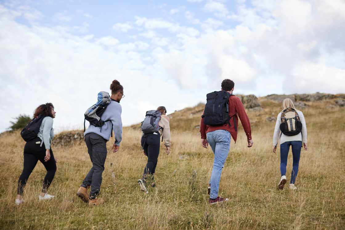 A group of five young adult friends hiking across a field towards the summit.