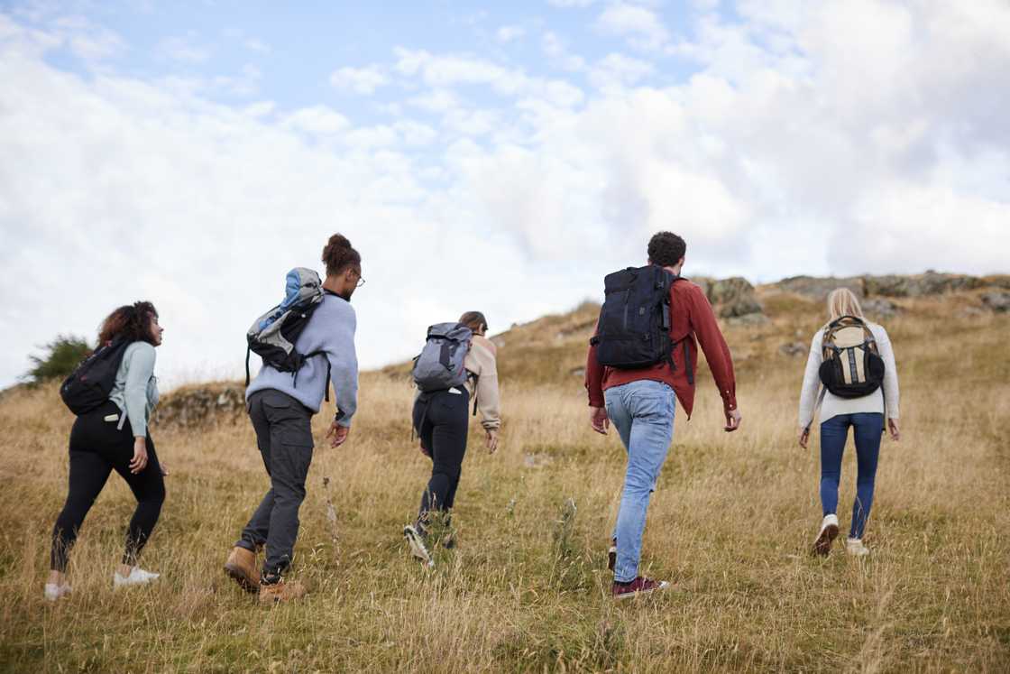 A group of five young adult friends hiking across a field towards the summit. A group of five young adult friends hiking across a field towards the summit.