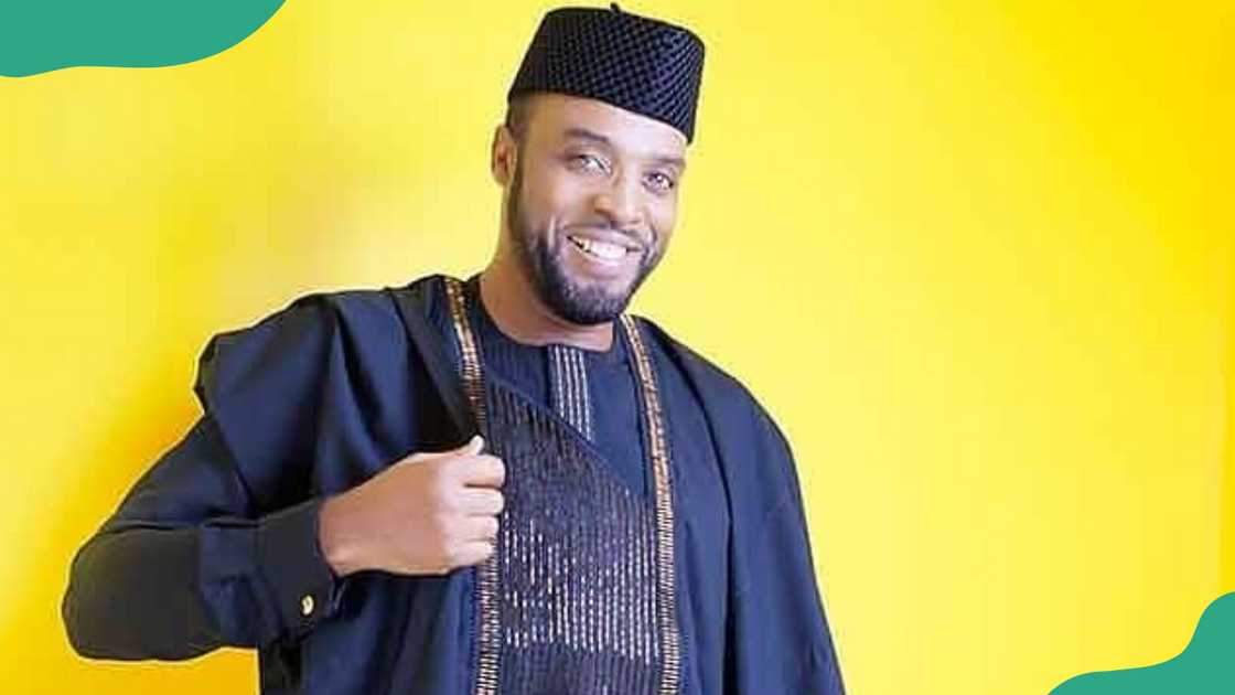 Kalu Ikeagwu poses for a picture in a black Agbada against a yellow background.