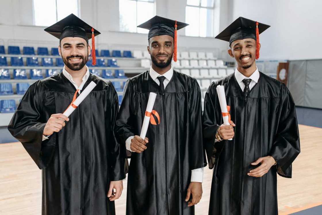 Men in academic dress standing while holding diplomat