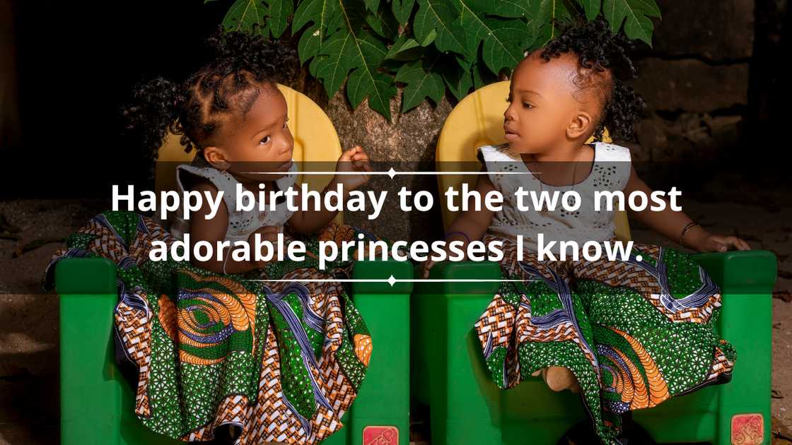 Little twin girls in colourful Ankara outfits are sitting on plastic chairs