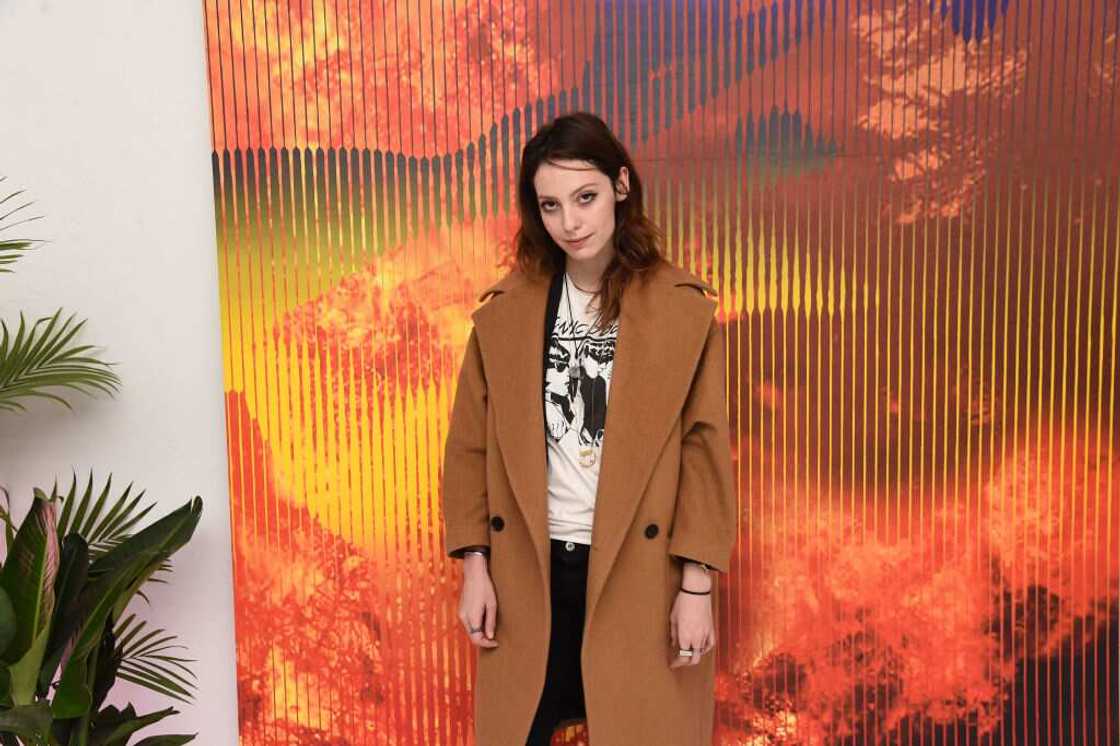 Cory Kennedy posing for a photo in a brown coat, white and black top and black pants