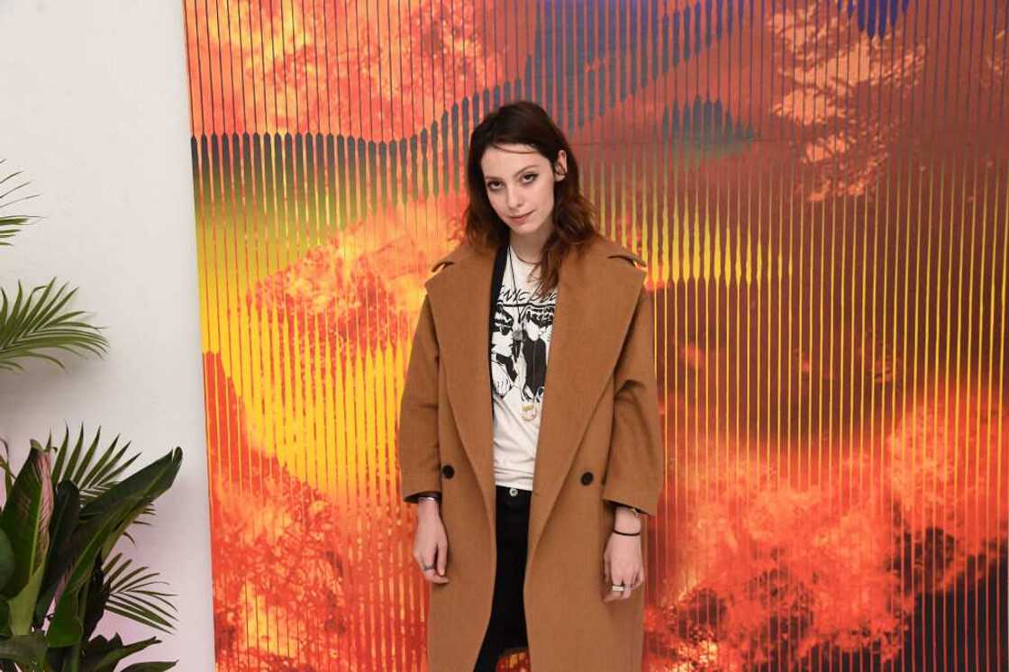 Cory Kennedy posing for a photo in a brown coat, white and black top and black pants Cory Kennedy posing for a photo in a brown coat, white and black top and black pants