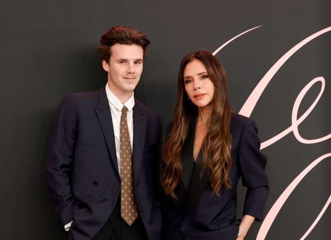 Cruz Beckham pose in a black suite, white shirt and a brown dotted tie (L) and Victoria Beckham in all black (R) Cruz Beckham pose in a black suite, white shirt and a brown dotted tie (L) and Victoria Beckham in all black (R)