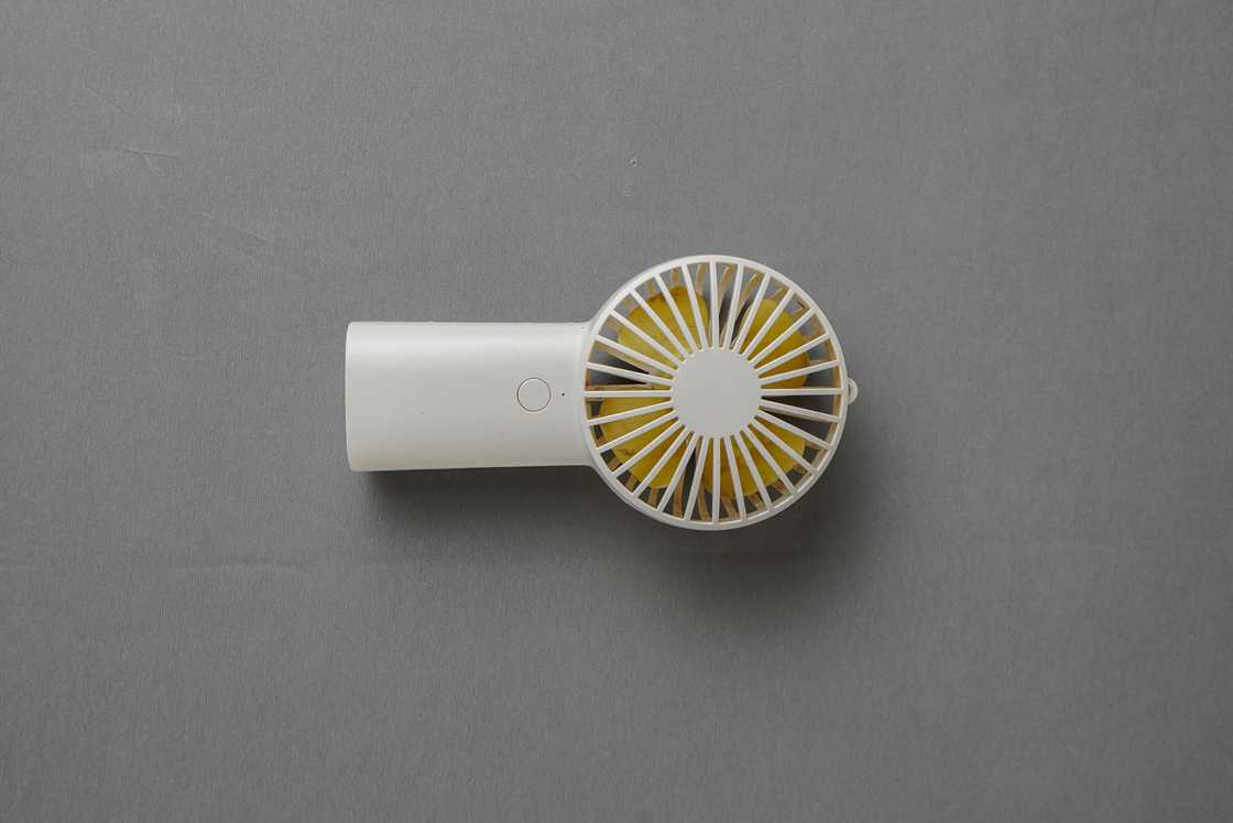 A white handheld cooling fan on a grey background A white handheld cooling fan on a grey background