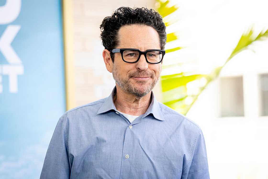 J.J. Abrams wearing black-framed glasses and a light blue button-up shirt, smiling outdoors with greenery in the background. J.J. Abrams wearing black-framed glasses and a light blue button-up shirt, smiling outdoors with greenery in the background.