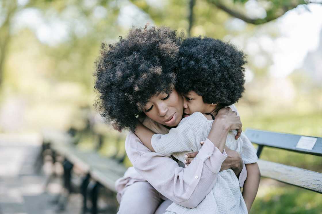 A mother hugging her young child on a park bench. A mother hugging her young child on a park bench.