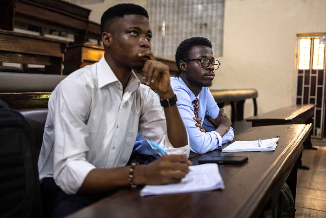 Two students listen attentively during a class session in a wood-panelled hall. Two students listen attentively during a class session in a wood-panelled hall.