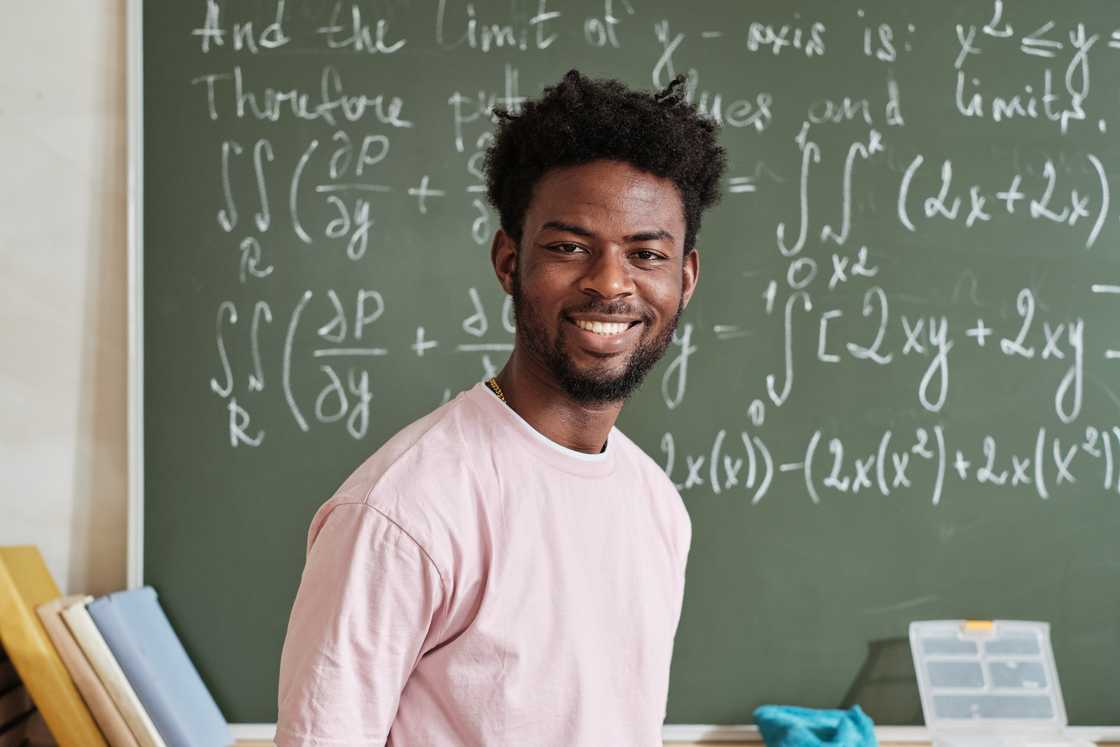A male student standing against the blackboard with maths formulas in the classroom. A male student standing against the blackboard with maths formulas in the classroom.