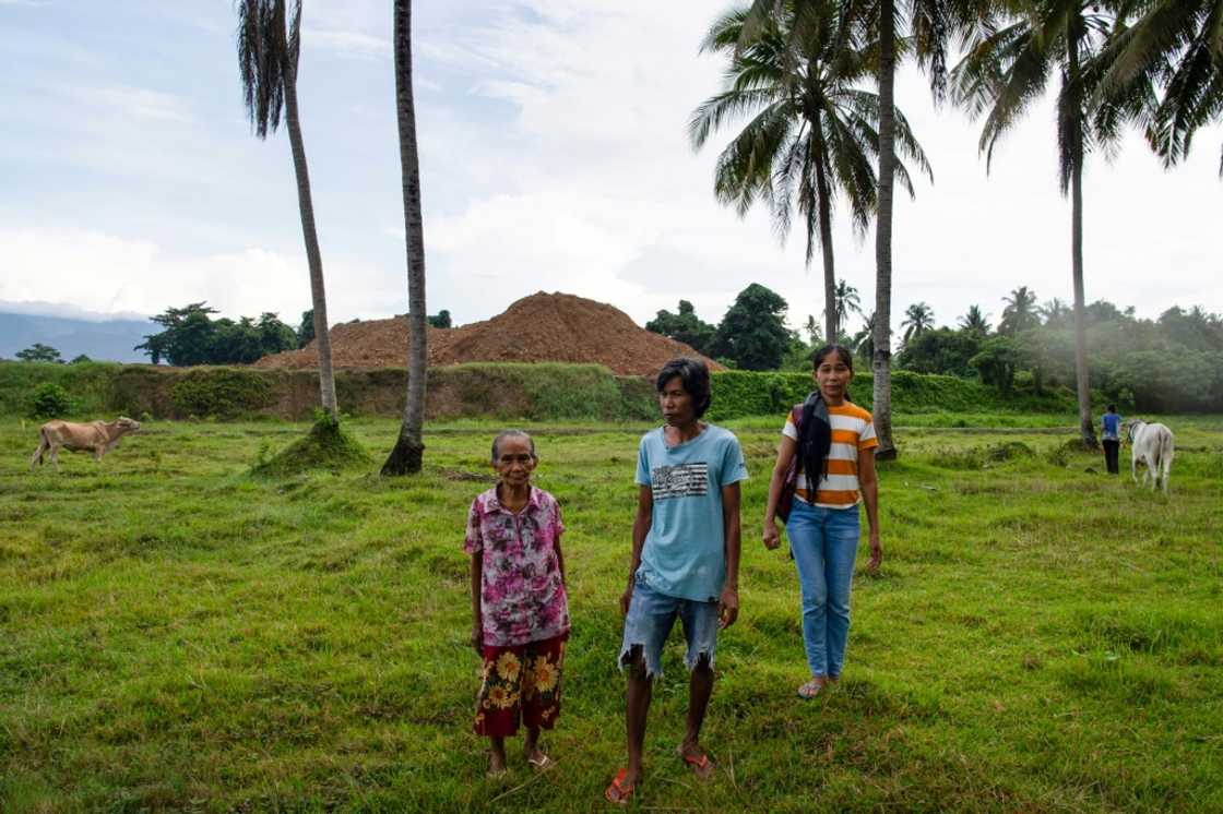 Moharen Tambiling (C), his sister Alayma (R) and their mother stand on their farm next to stockpiled nickel ore in Palawan province