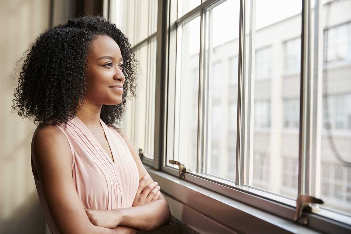 Young black woman with arms crossed looking out of window Young black woman with arms crossed looking out of window