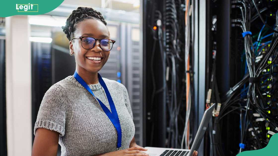 A young woman using a laptop in a server room A young woman using a laptop in a server room