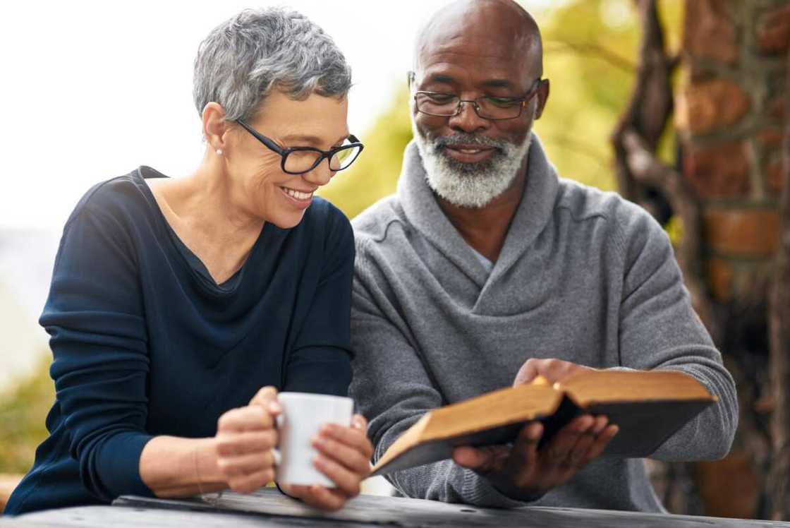 An affectionate senior couple reading their bible while sitting outside An affectionate senior couple reading their bible while sitting outside