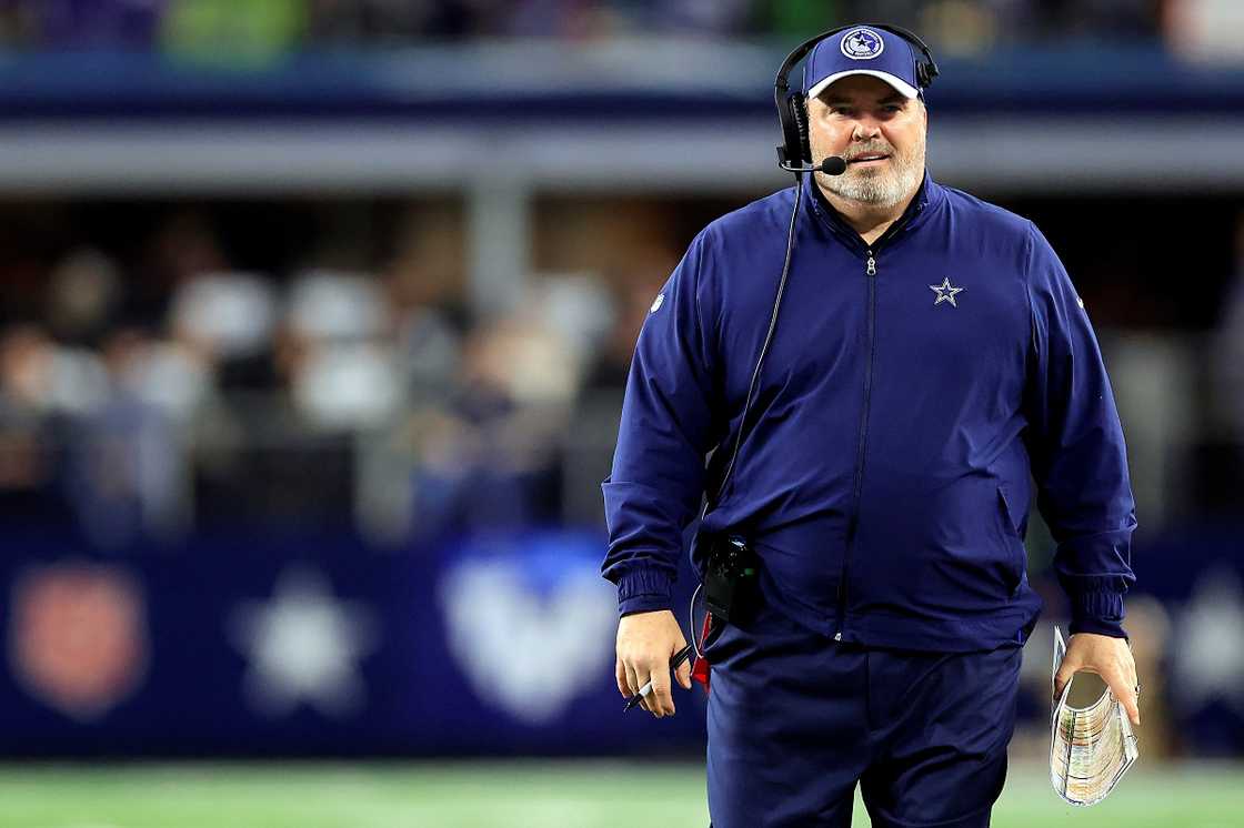 Mike McCarthy walks on a field in a blue outfit during a football match.