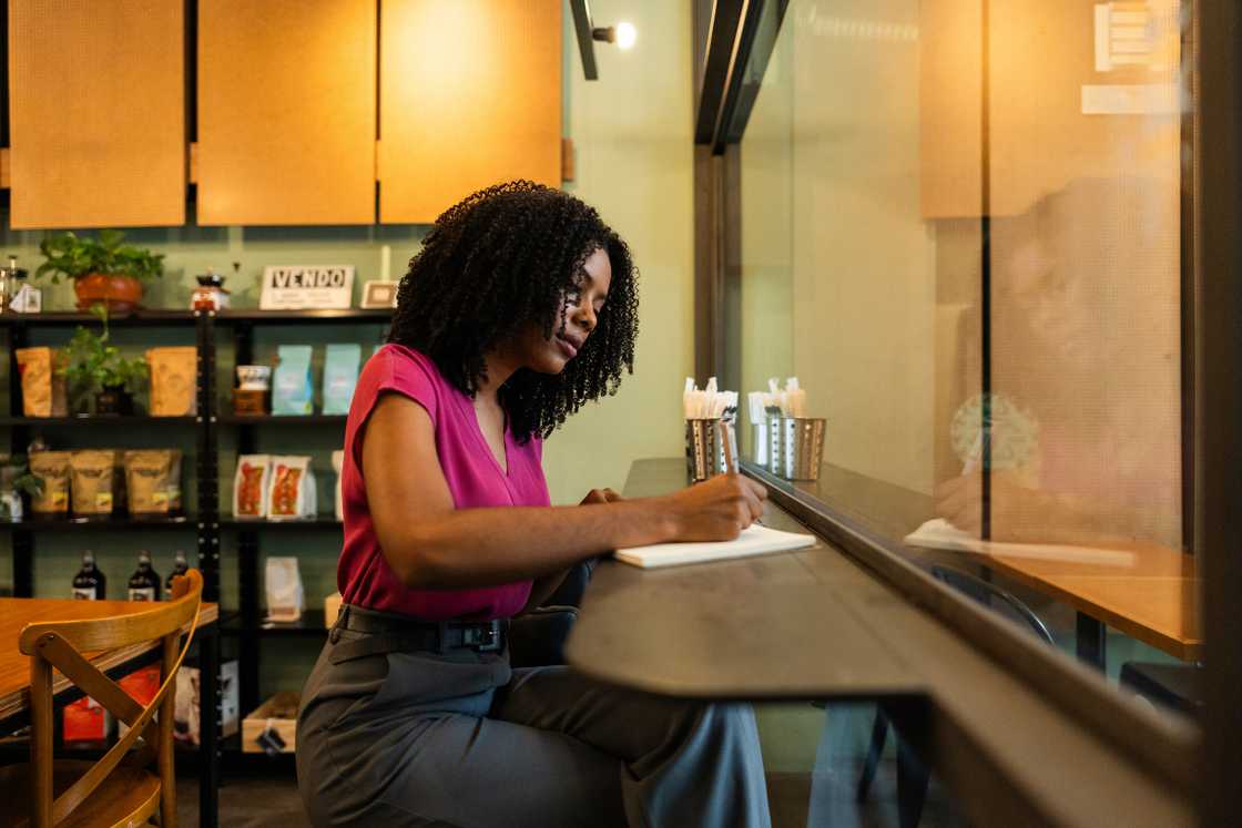 A woman writing in a notebook at a bagel shop table.