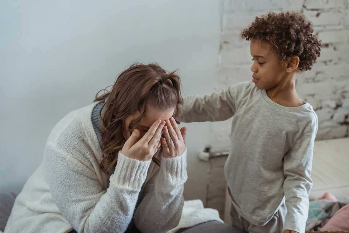 A child comforting a crying woman sitting on a bed. A child comforting a crying woman sitting on a bed.
