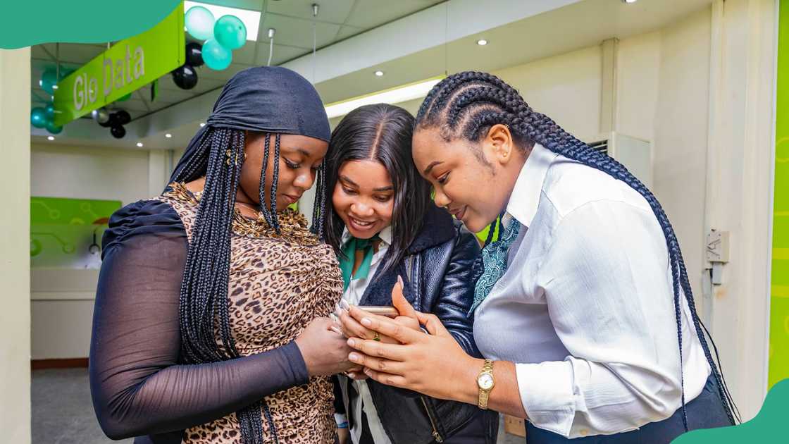 Three young women working with Glo looking at a phone. Three young women working with Glo looking at a phone.