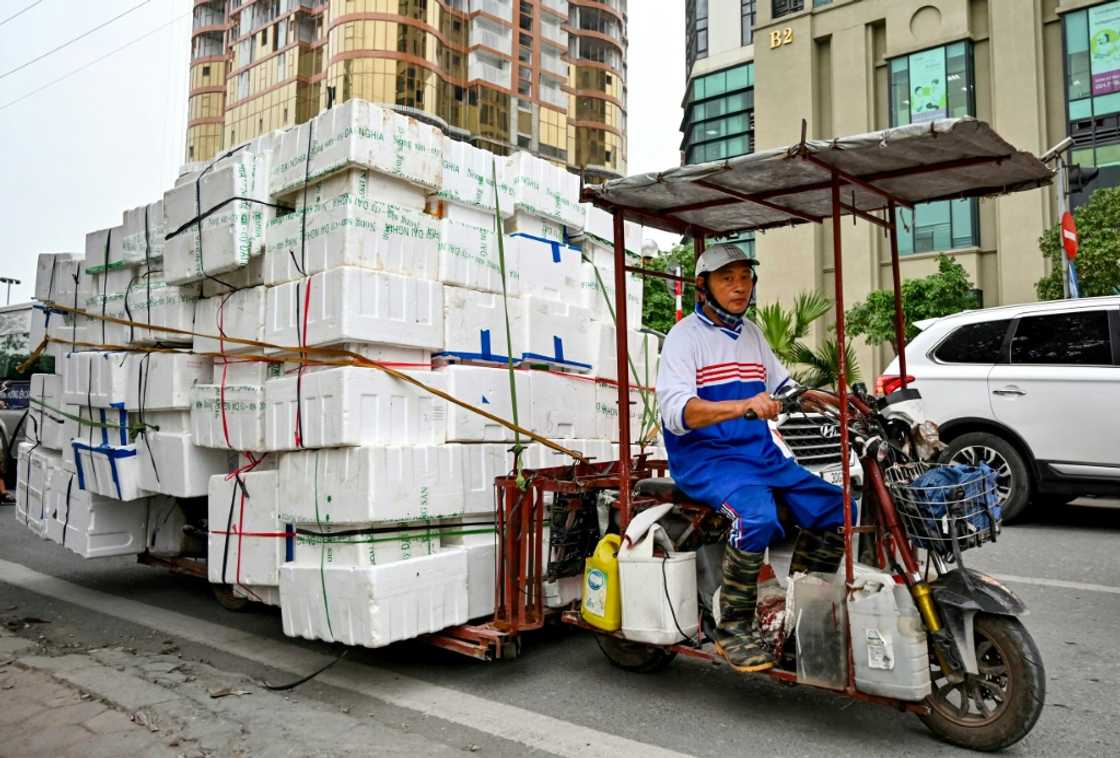 A man rides an electric motorbike carrying foam sheets on a street in Hanoi