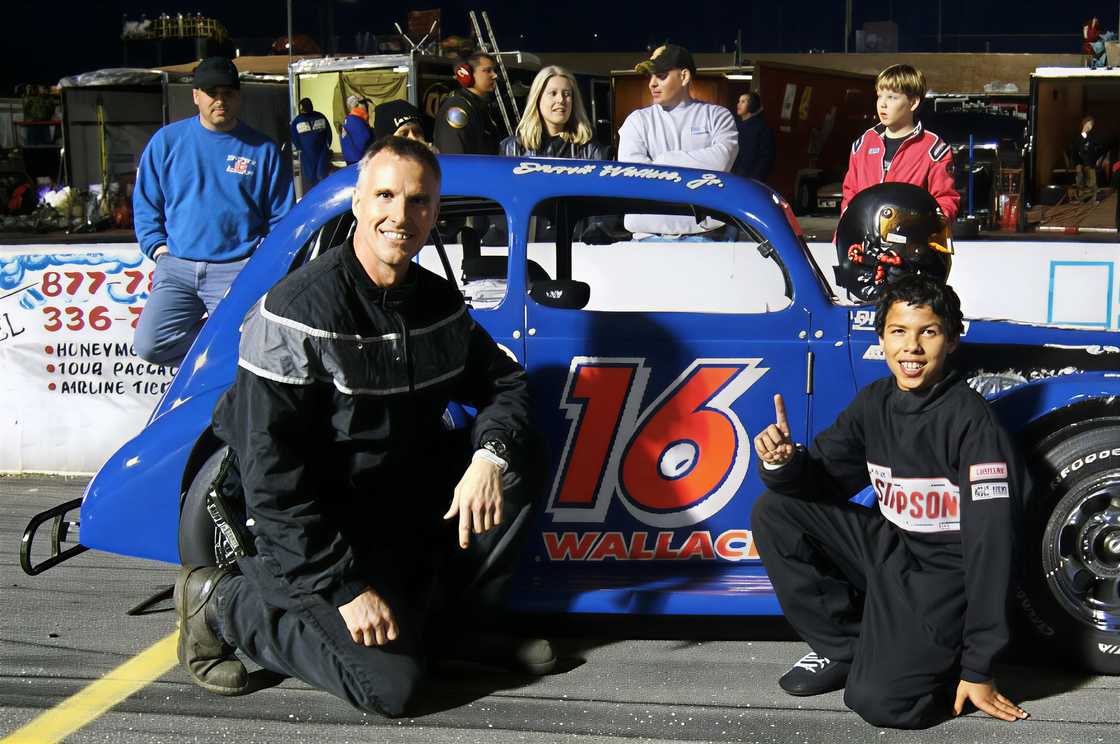 Bubba Wallace and his father Darrell Wallace, Jr. pose next to a race car Bubba Wallace and his father Darrell Wallace, Jr. pose next to a race car