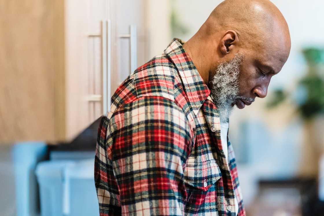A man with a bald head and a grey beard looks downward.