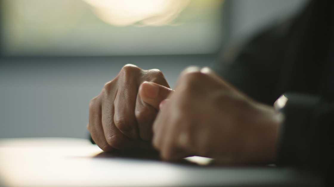 Two hands rest together on a table in soft light.