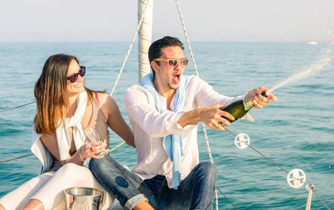 A couple in love on sailing boat cheering with champagne wine bottle for a birthday party cruise travel on luxury sailboat