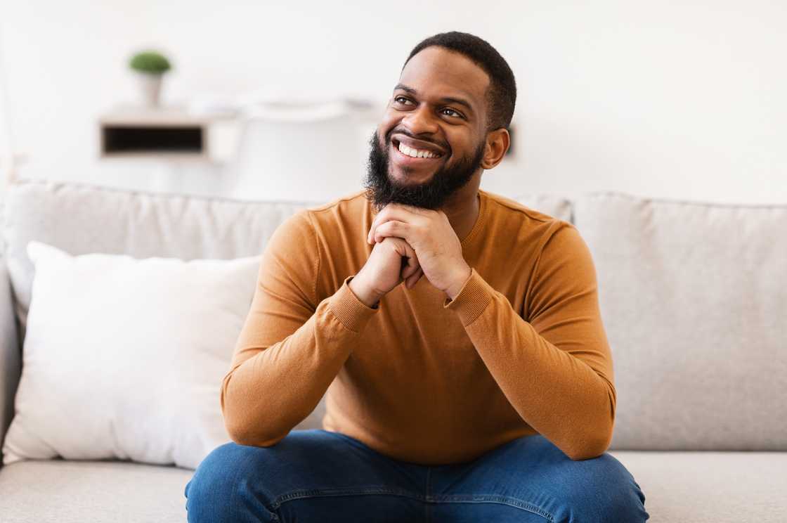 A man thinking and smiling while sitting on the couch at home. A man thinking and smiling while sitting on the couch at home.