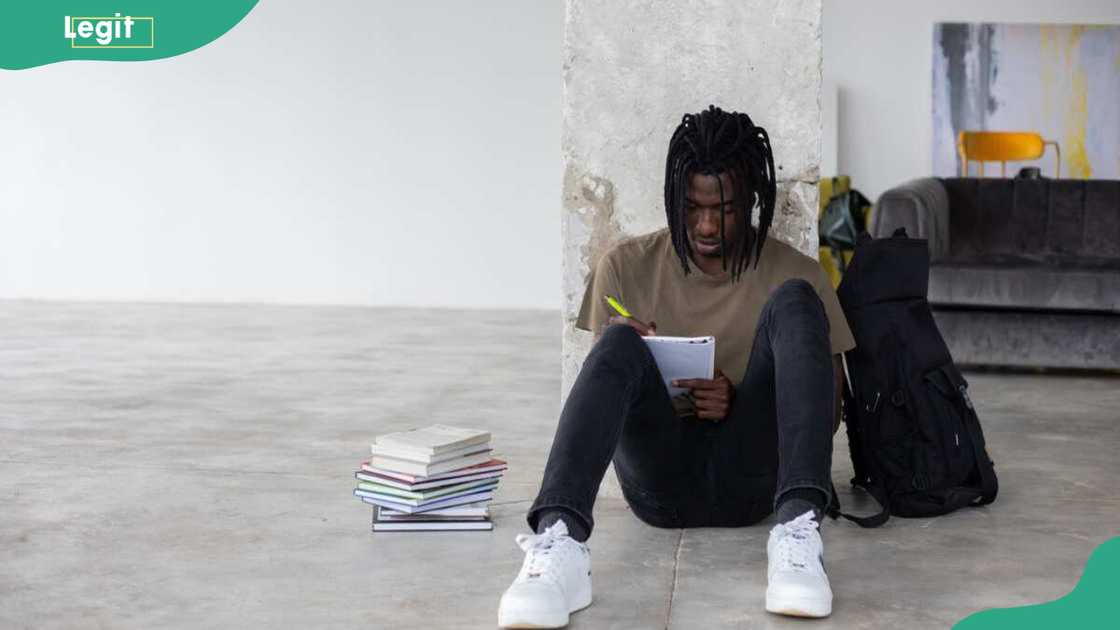 A student writing in a note book while sitting on a floor. A student writing in a note book while sitting on a floor.