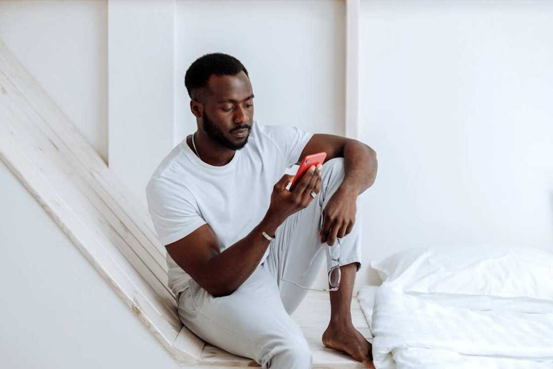 A man using a phone while sitting on a white surface A man using a phone while sitting on a white surface