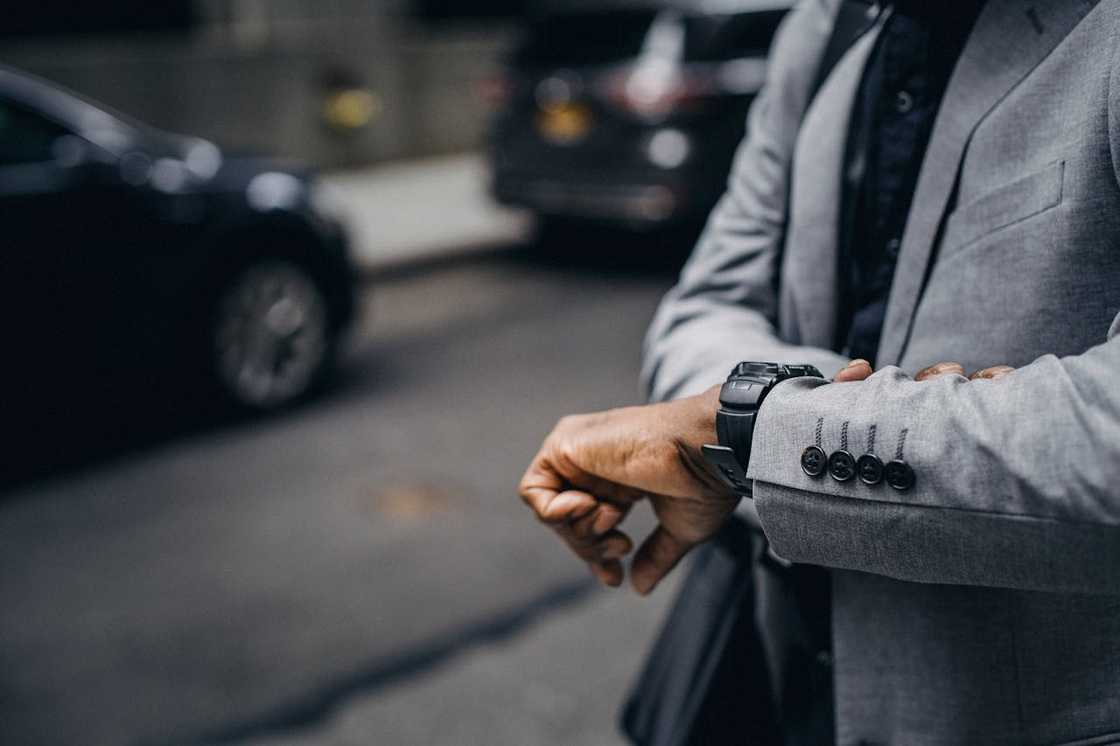 A man in a suit checking his wristwatch outdoors.