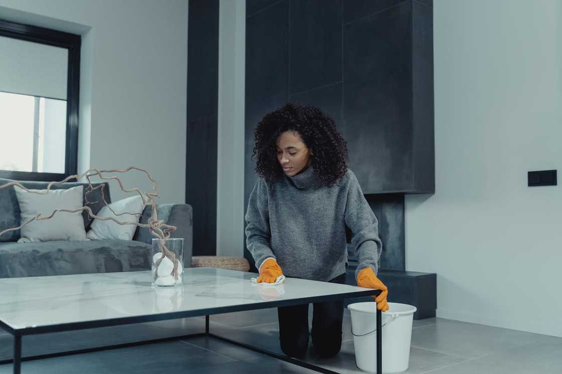 A woman in grey sweater cleans and arranges the living room.