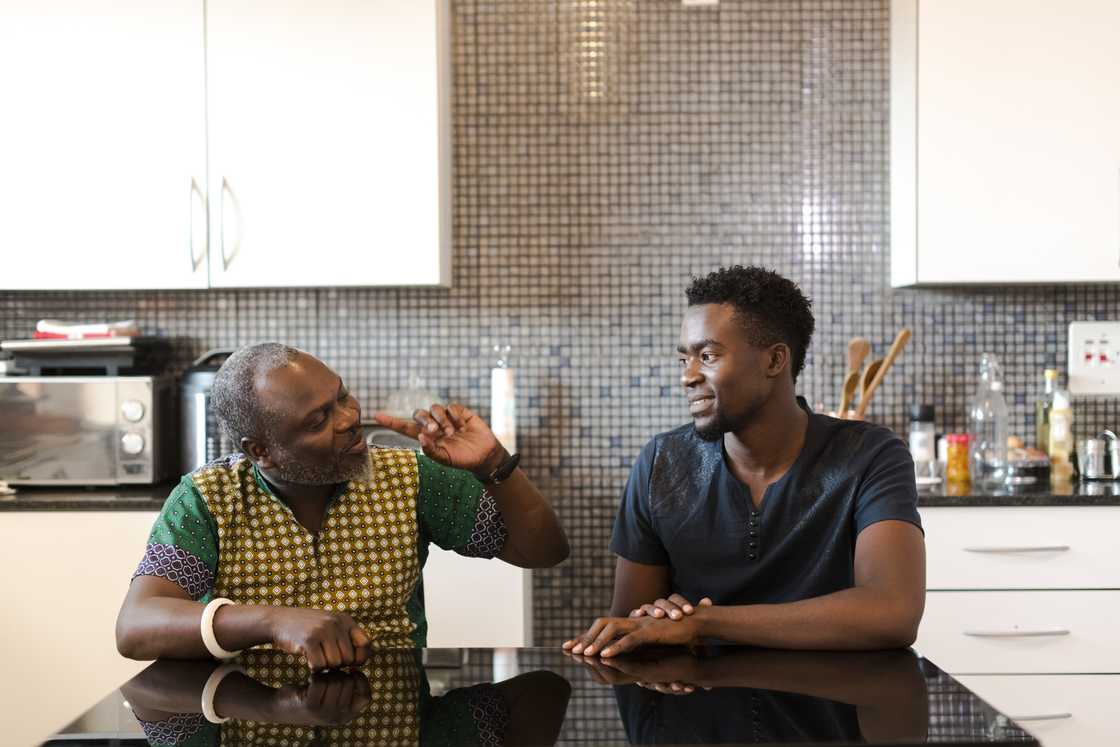 Adult child and father locked in a silent standoff in the kitchen.