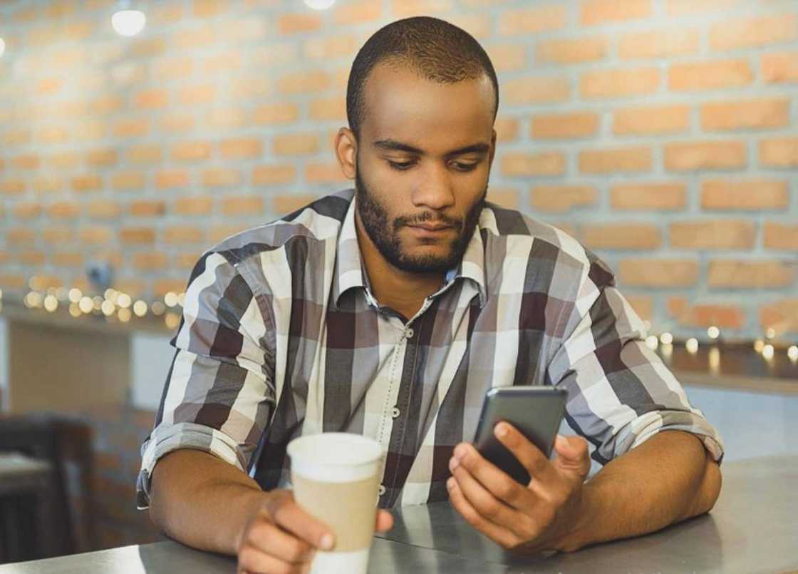 A customer using his mobile phone as he takes coffee A customer using his mobile phone as he takes coffee