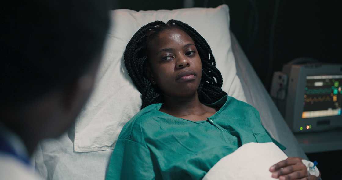 A woman rests on a bed with an IV drip.