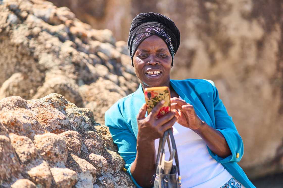 A woman uses her phone while leaning on a rock