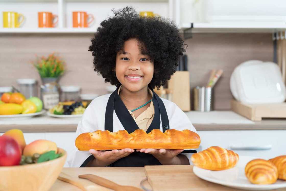 A girl holding bread big in the kitchen.