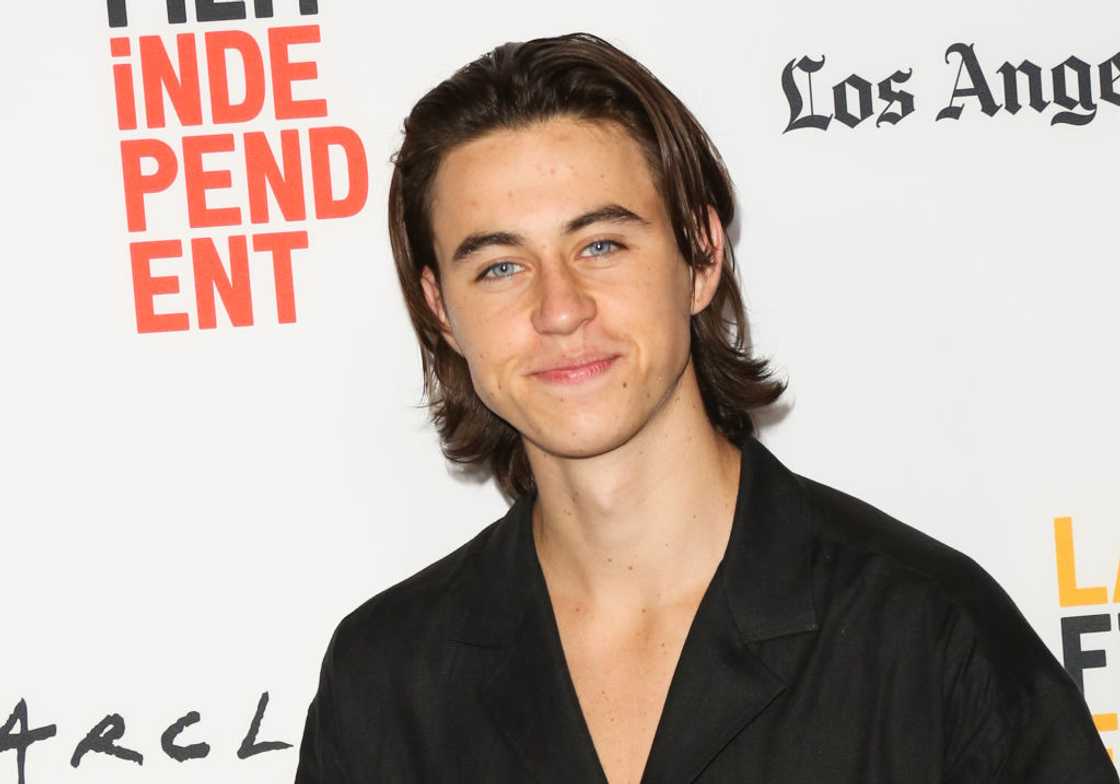 Nash Grier with shoulder-length brown hair poses in a black shirt in front of a Los Angeles Film Independent backdrop.