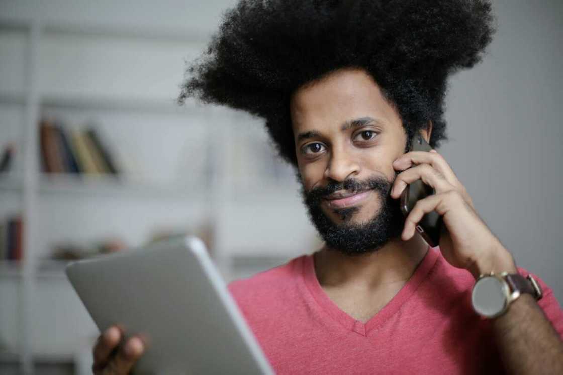 A young man is using a smartphone while holding a tablet