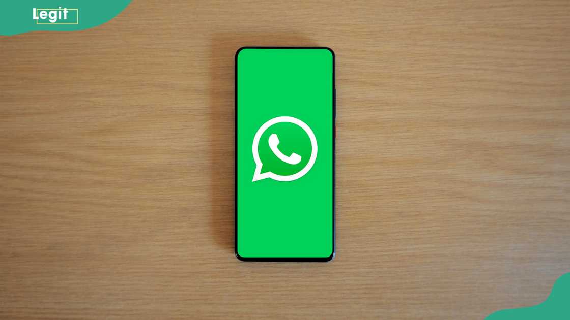 A cellphone with a WhatsApp logo on the screen on a wooden background A cellphone with a WhatsApp logo on the screen on a wooden background