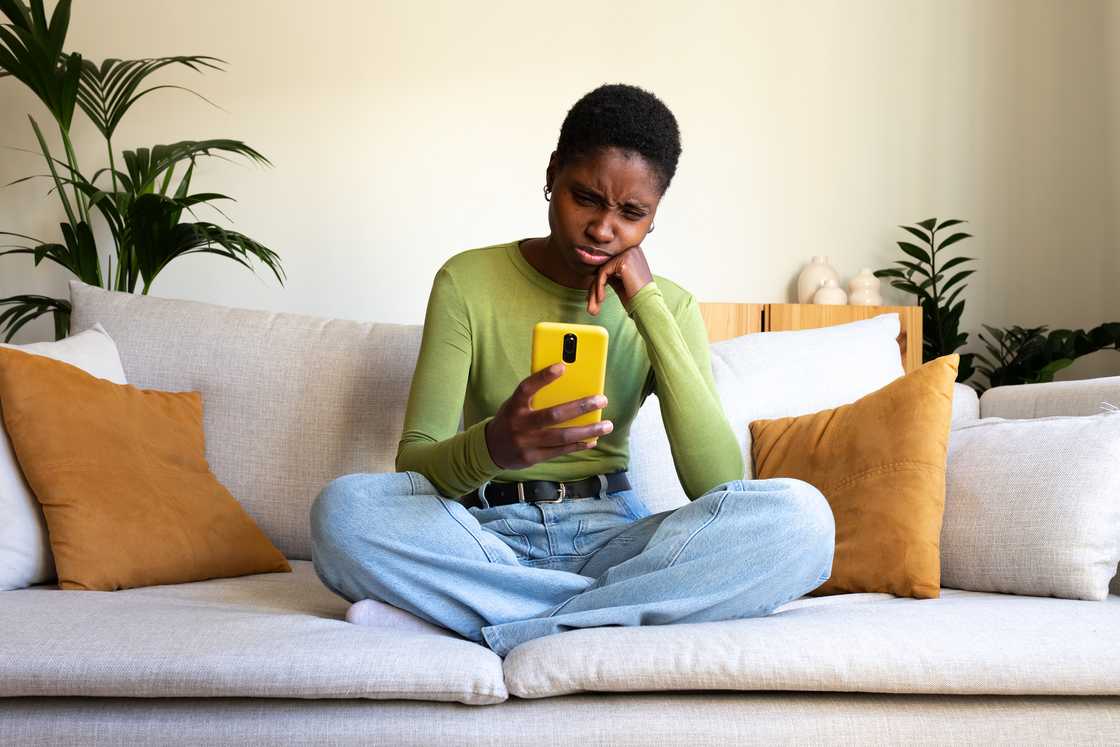 A young woman sitting on a sofa and looking at a smartphone.