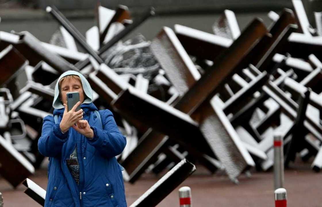 A woman takes a selfie in front of anti-tank constructions covered with snow after the first snow falls of the season, in Kyiv