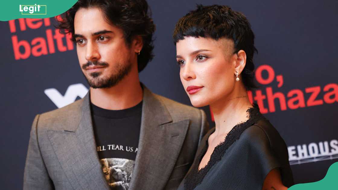A couple pose closely at a film premiere, the man in a grey blazer and the woman with a cropped black hairstyle.