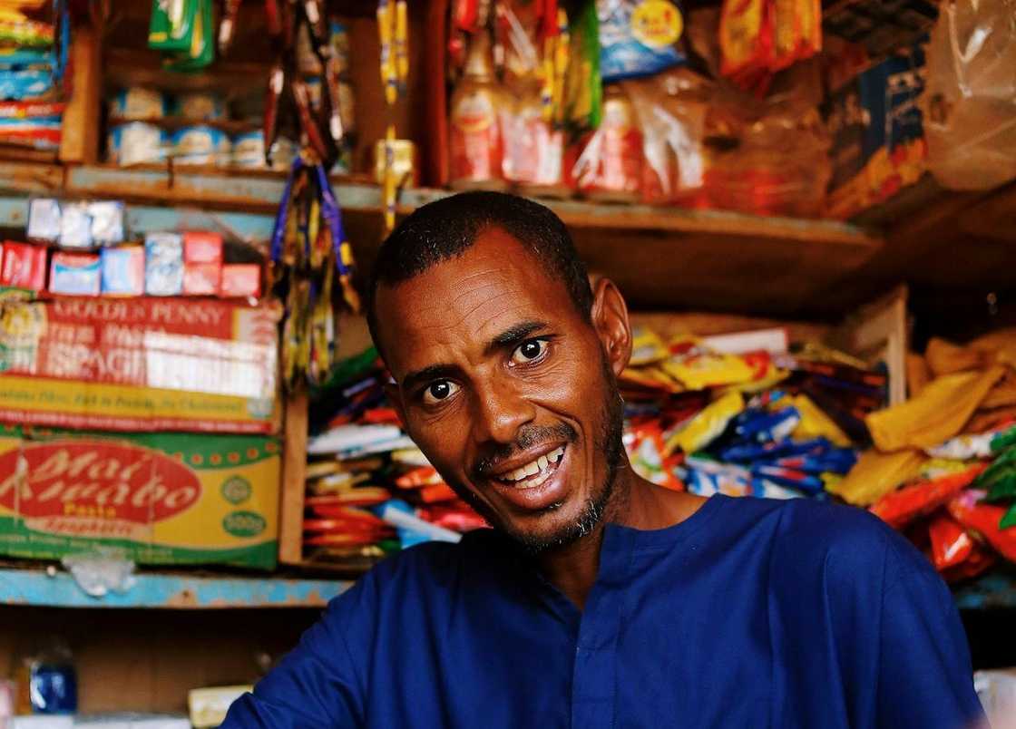 A smiling shop owner standing inside a packed neighbourhood shop.