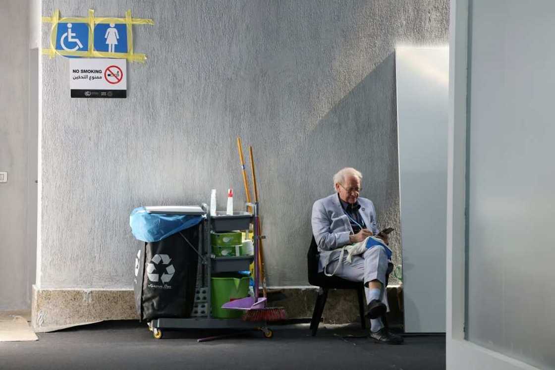 A delegate checks his mobile on Novmeber 15, 2022 next to a cleaners' trolley during the COP27 climate conference.